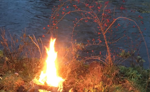 Ein Feuer am Ufer eines Flusses mit einem Hagebuttenast.
