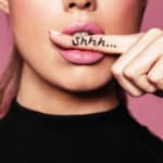 Ein halbes Frauengesicht mit einem Finger quier im Mund, auf dem Shhh steht