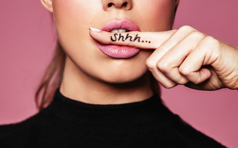 Ein halbes Frauengesicht mit einem Finger quier im Mund, auf dem Shhh steht