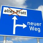blaue Strassenanzeigetafel. Darauf steht ein Wegweiser mit Alter Trott geradeaus und ein Pfeil rechts ab Neuer Weg. Neuer Weg: Gewaltfreie Kommunikation und Wertschätzung