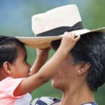 Frau mit Kind auf dem Arm. Das Kind hält einen Strohhut über den Kopf der Frau. Kommunikation mit dem inneren Kind.